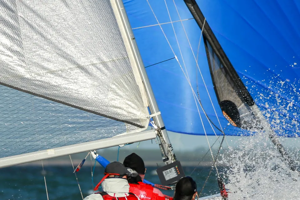Photo composite: a SailNav display mounted on the mast of a sportboat racing under a blue spinnaker in spray